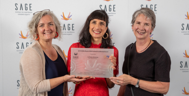 Three women from La Trobe University holding their institution's Athena Swan Bronze Award plaque.