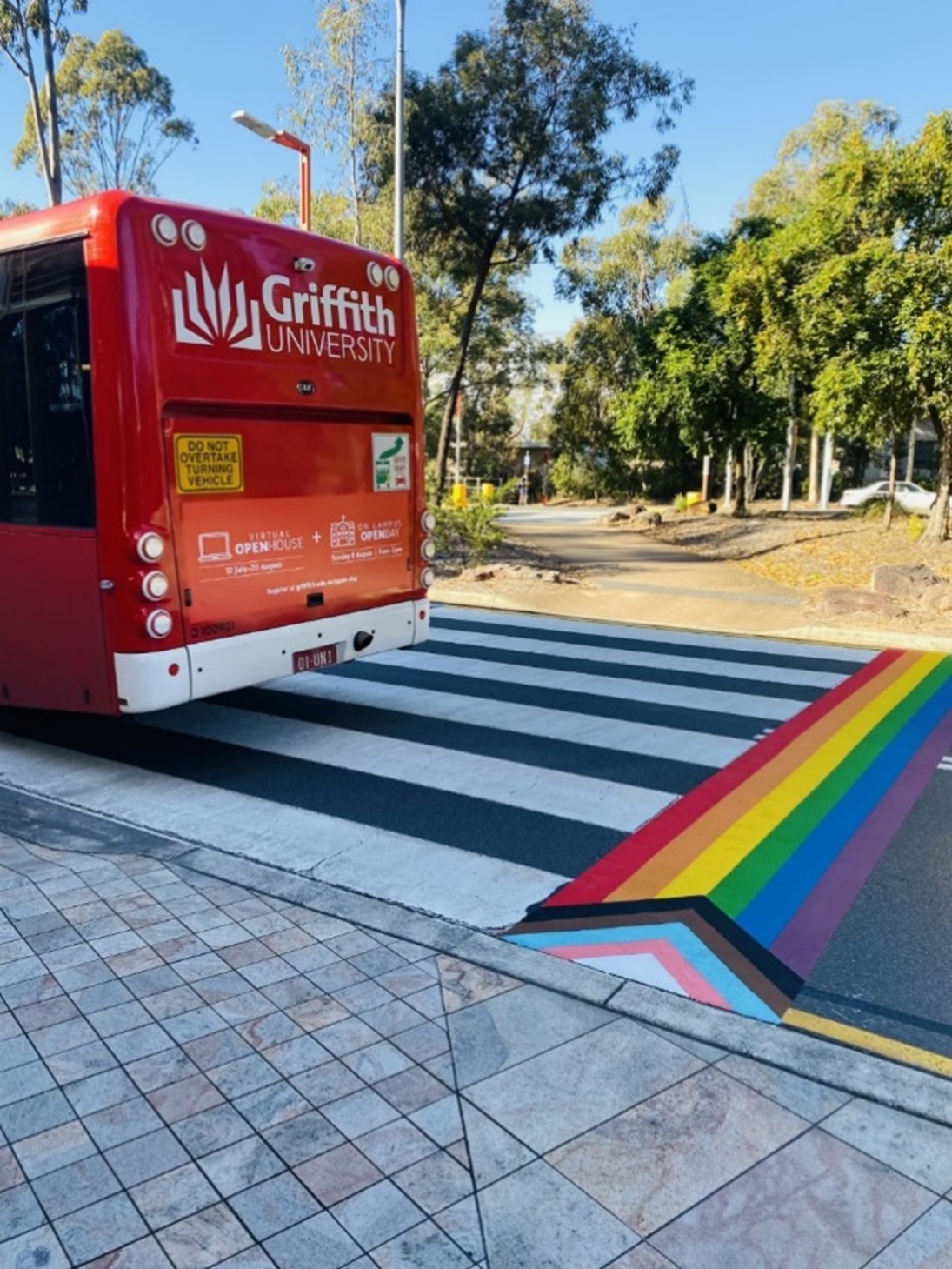 A Griffith University bus drives over a pedestrian crossing on which a Progress Pride Flag has been painted.