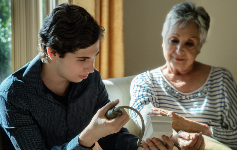 A young man helps his elderly grandmother use a blood pressure cuff.