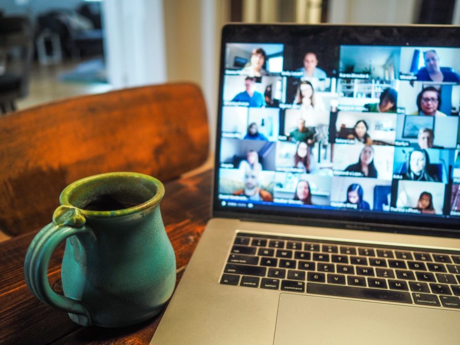 Laptop displaying a group of people in an online meeting, with a green mug to the left side.