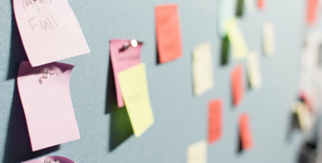 Pinboard covered in post-it notes, with one saying 'impact'